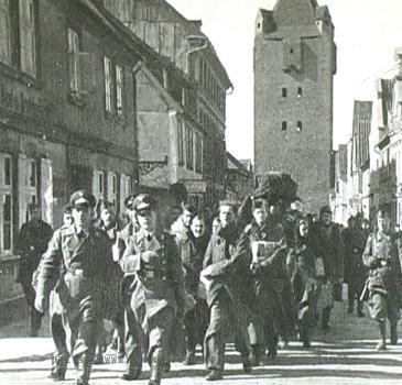 POWs are marched to Stalag Luft I from the railroad station through the town of Barth  En route they pass through the Dammtor Gate  as seen in the background of this photo  The gate